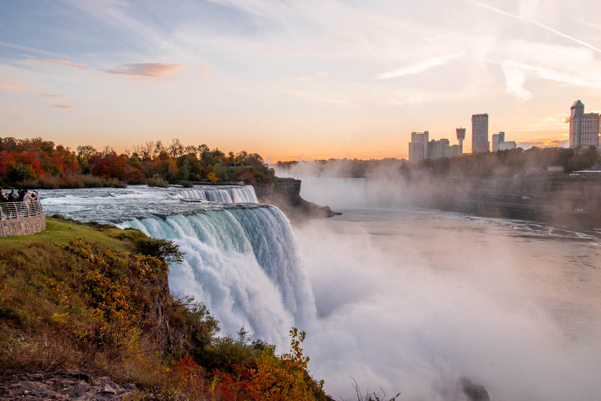 Majestic view of the American Falls at sunset with mist rising and autumn trees glowing in warm hues.