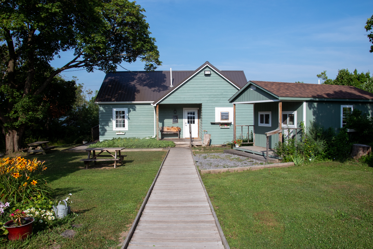 Exterior of Elf in the Oak, a quaint green building with a wooden walkway, picnic tables, and garden flowers.