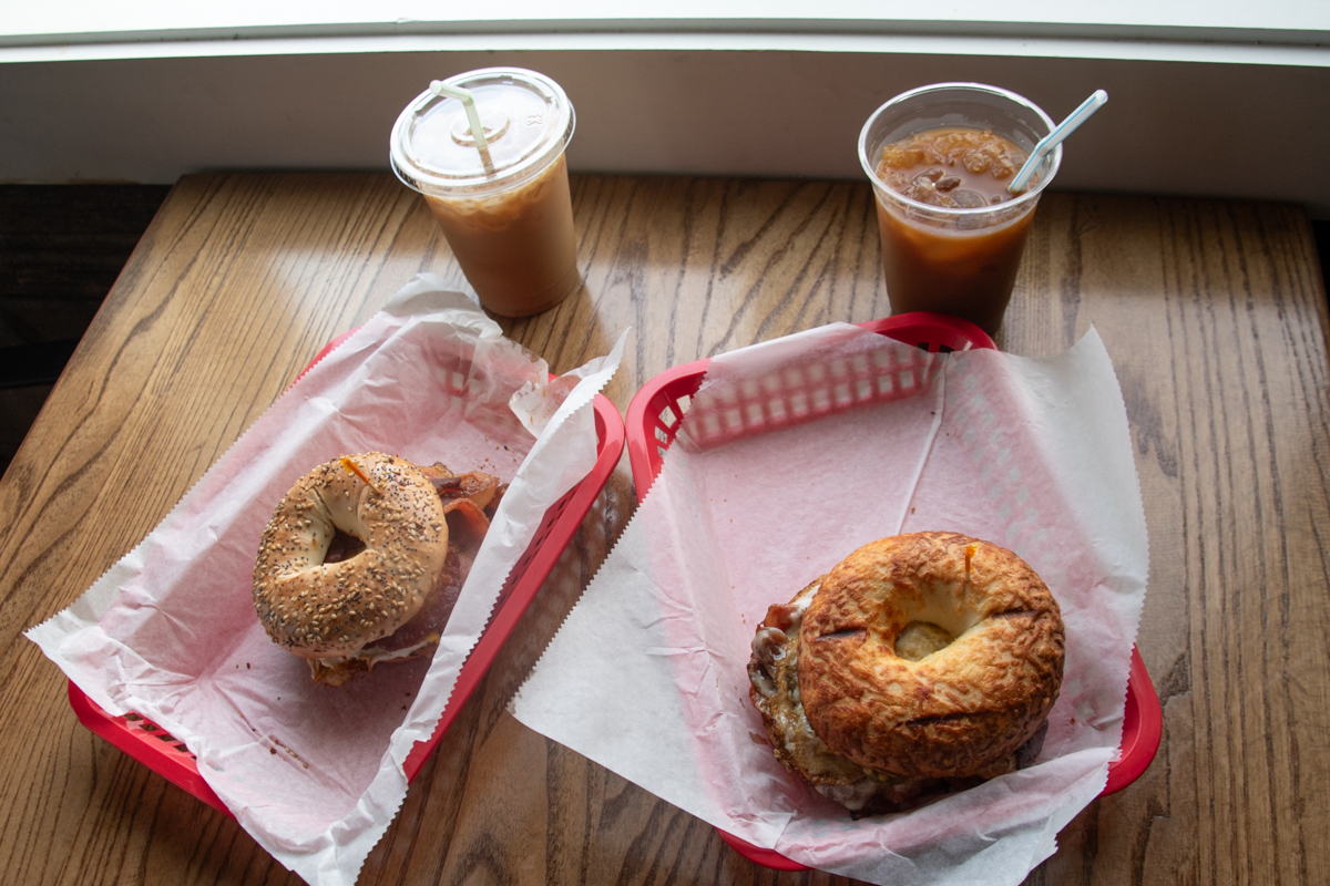Breakfast at Elf in the Oak featuring two iced coffees and two bagel sandwiches in red baskets on a wooden table.