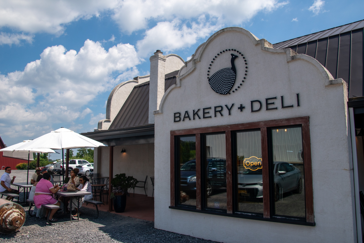 Exterior of Tabora Farm and Winery’s bakery and deli with outdoor seating under white umbrellas.
