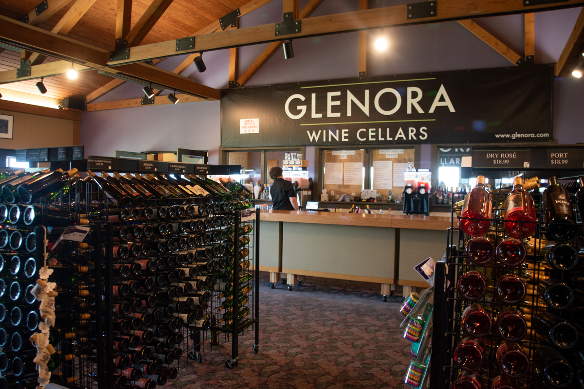 Interior of Glenora Wine Cellars tasting room with racks of wine bottles and a large sign above the tasting counter.