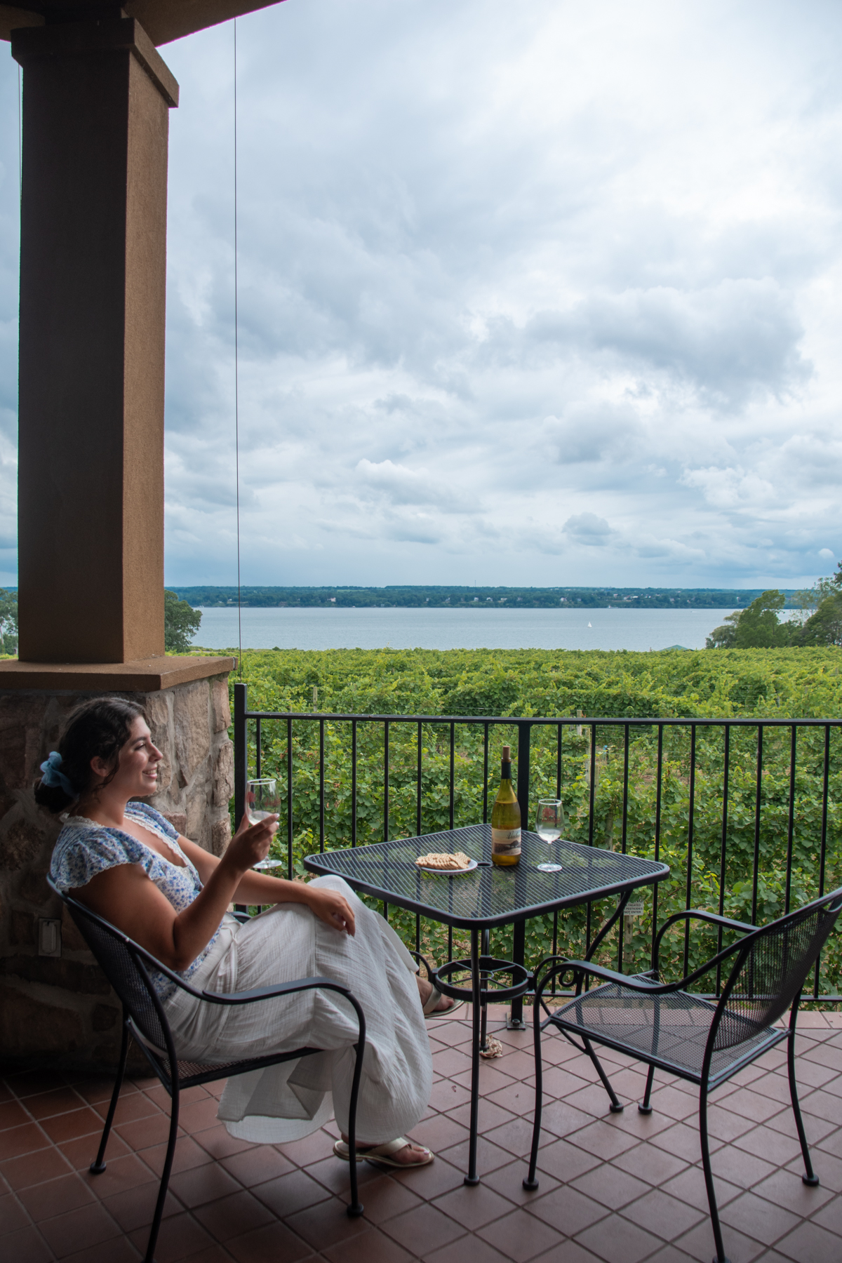 girl sitting with wine glass in front of vineyard with lake view