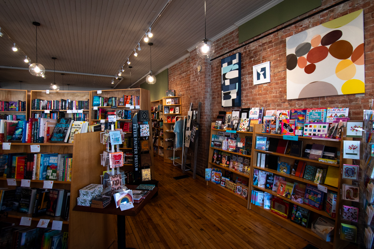 Act 4 Books bookstore in Perry, New York – Interior view of Act 4 Books featuring shelves filled with novels, children’s books, and gifts, with brick walls and modern art creating a warm, inviting atmosphere.