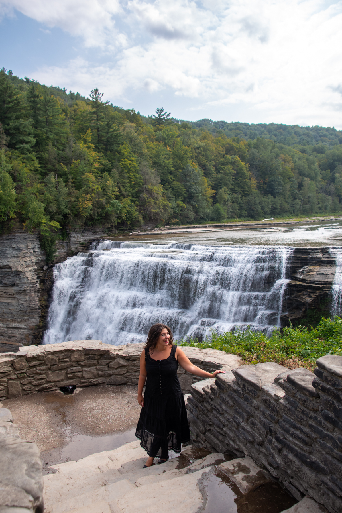 Visitor at waterfall overlook steps – woman in black dress standing along stone steps with Middle Falls flowing behind her.