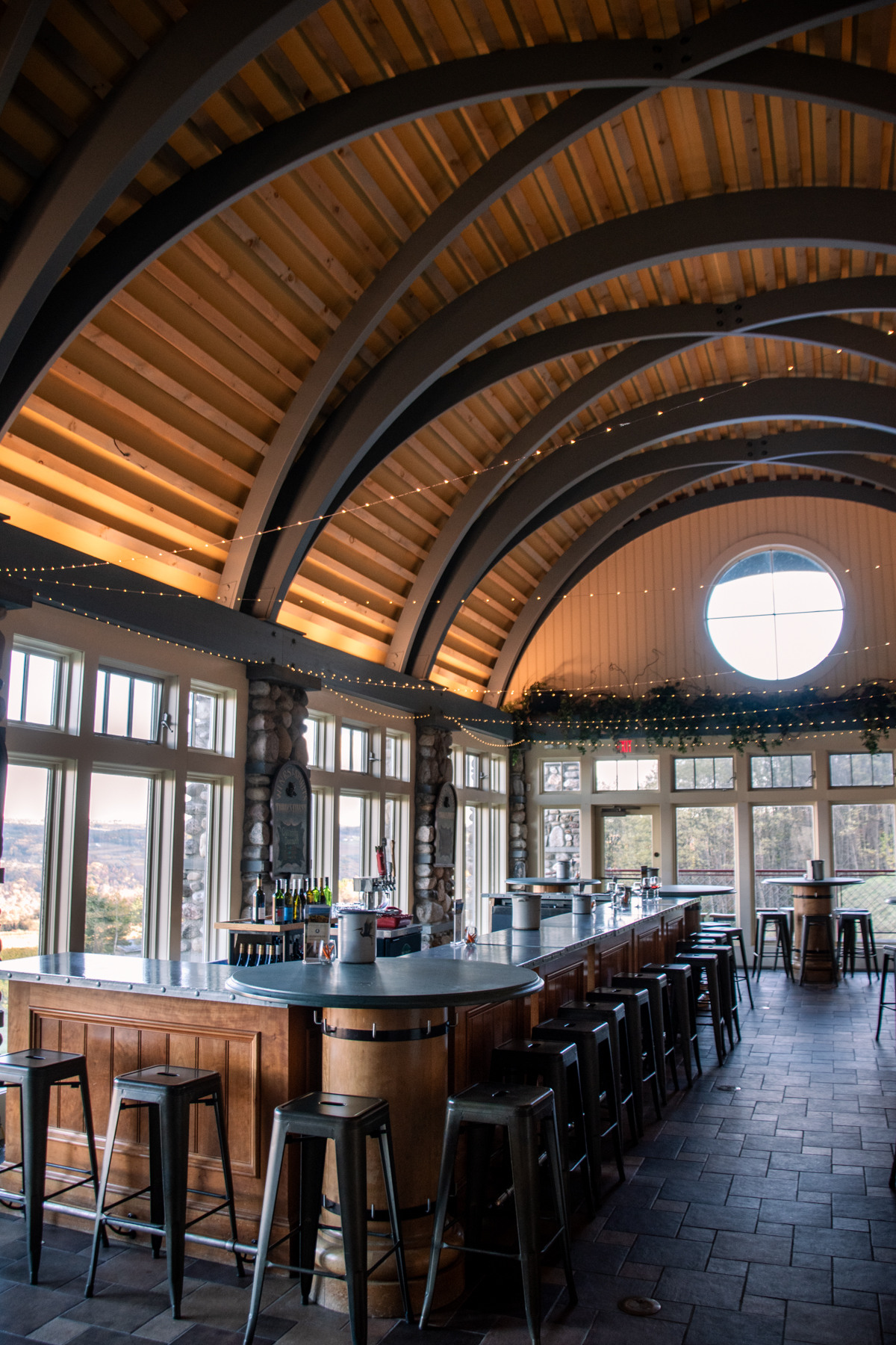 Interior of the Heron Hill Winery tasting room featuring high arched wooden ceilings, stone accents, and wraparound windows with views of the vineyards.