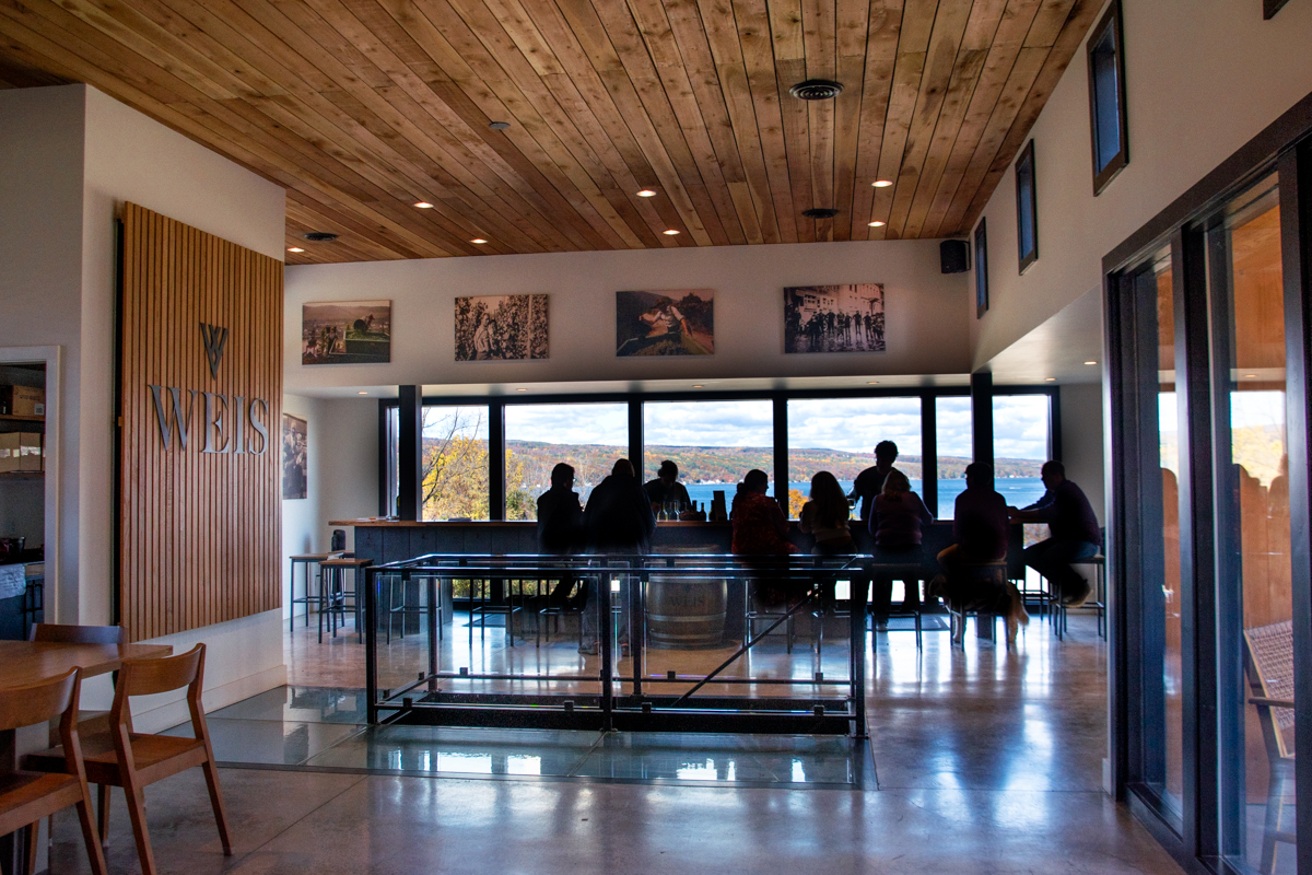 Guests seated inside the Weis Vineyards tasting room, enjoying panoramic views of Keuka Lake through floor-to-ceiling windows