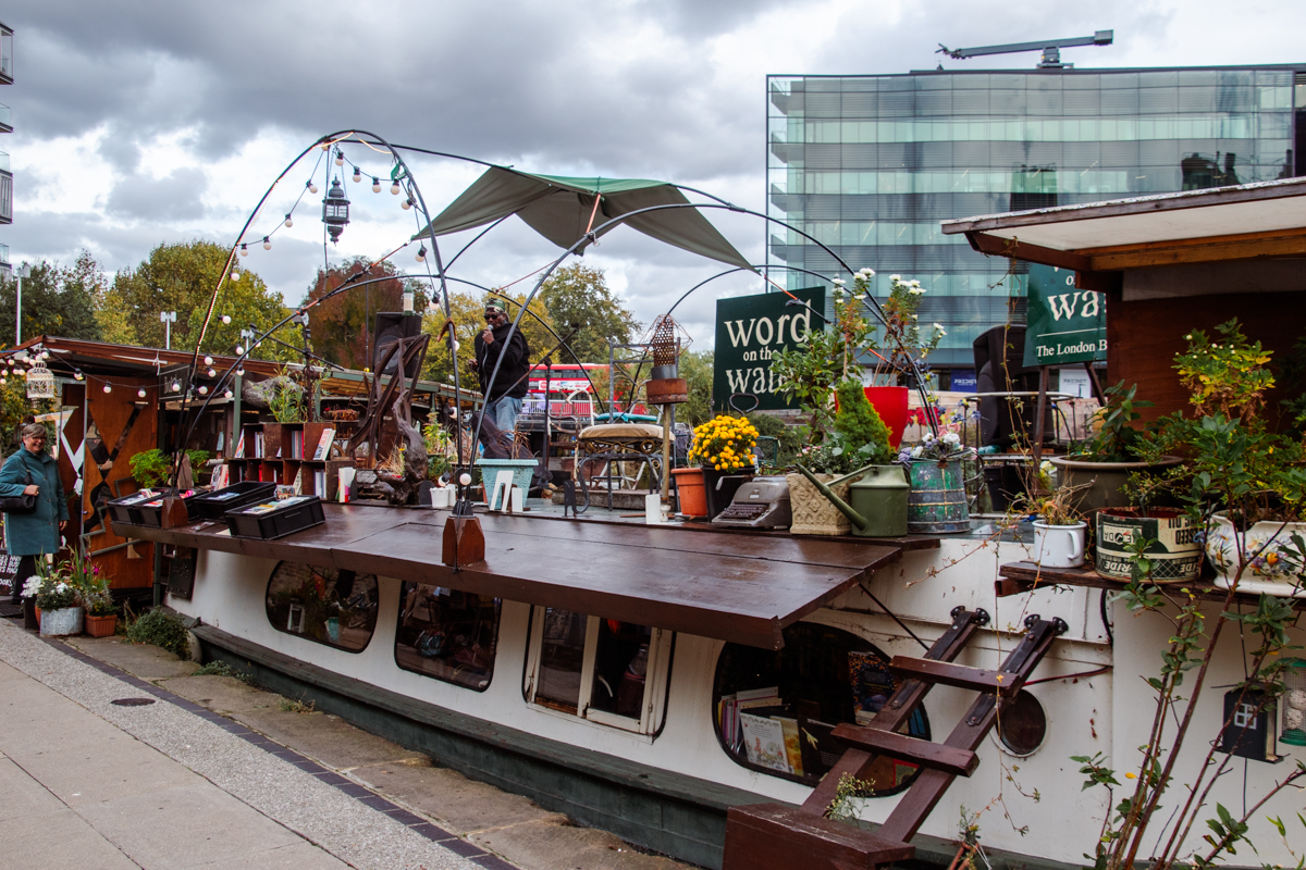 Exterior of Word on the Water floating bookstore moored on Regent’s Canal in London, with musician performing on deck