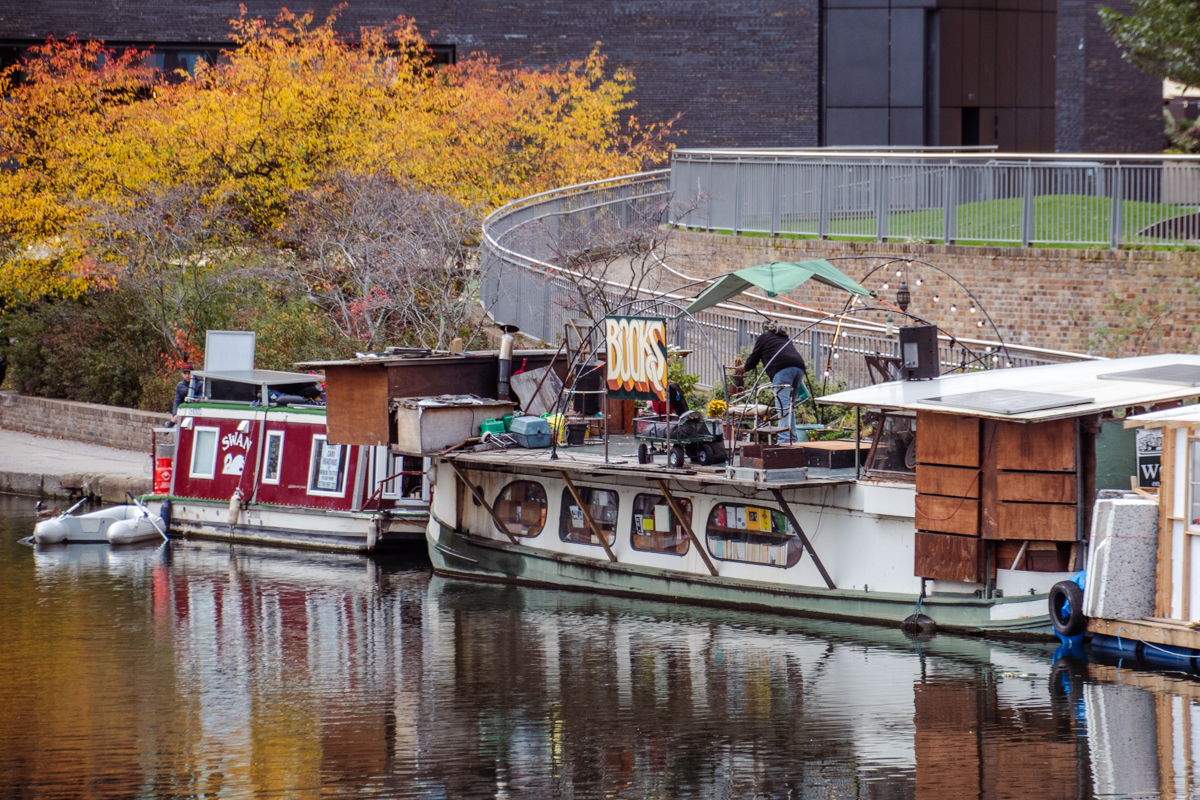Autumn scene of Word on the Water, a floating bookstore moored on Regent’s Canal in London, surrounded by houseboats and golden trees