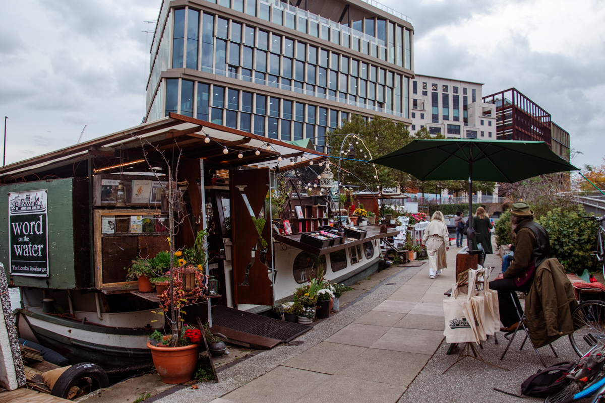 View of the Word on the Water floating bookstore moored along Regent’s Canal with visitors walking past near King’s Cross