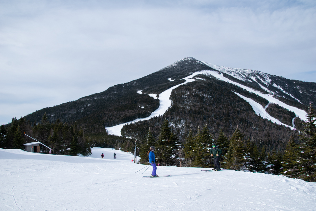 Skiers descending a snow-covered trail at Whiteface Mountain with Adirondack peaks in the background
