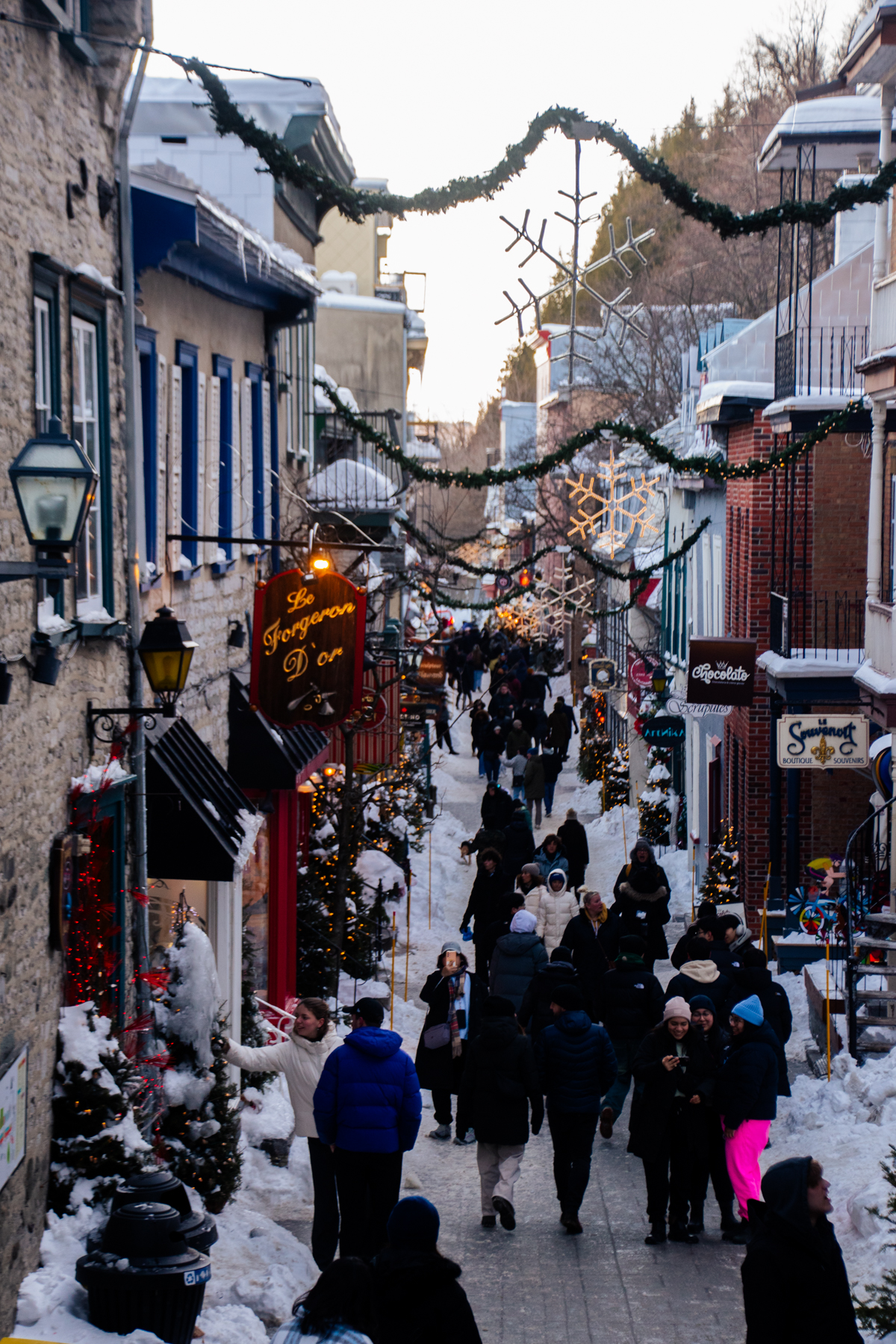 Crowds walking along Rue du Petit-Champlain decorated with garlands and snowflakes in Old Quebec City during winter.