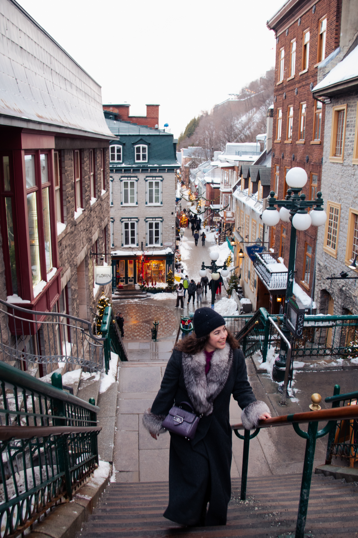 Woman walking down Breakneck Stairs toward Rue du Petit-Champlain in Old Quebec City during winter.