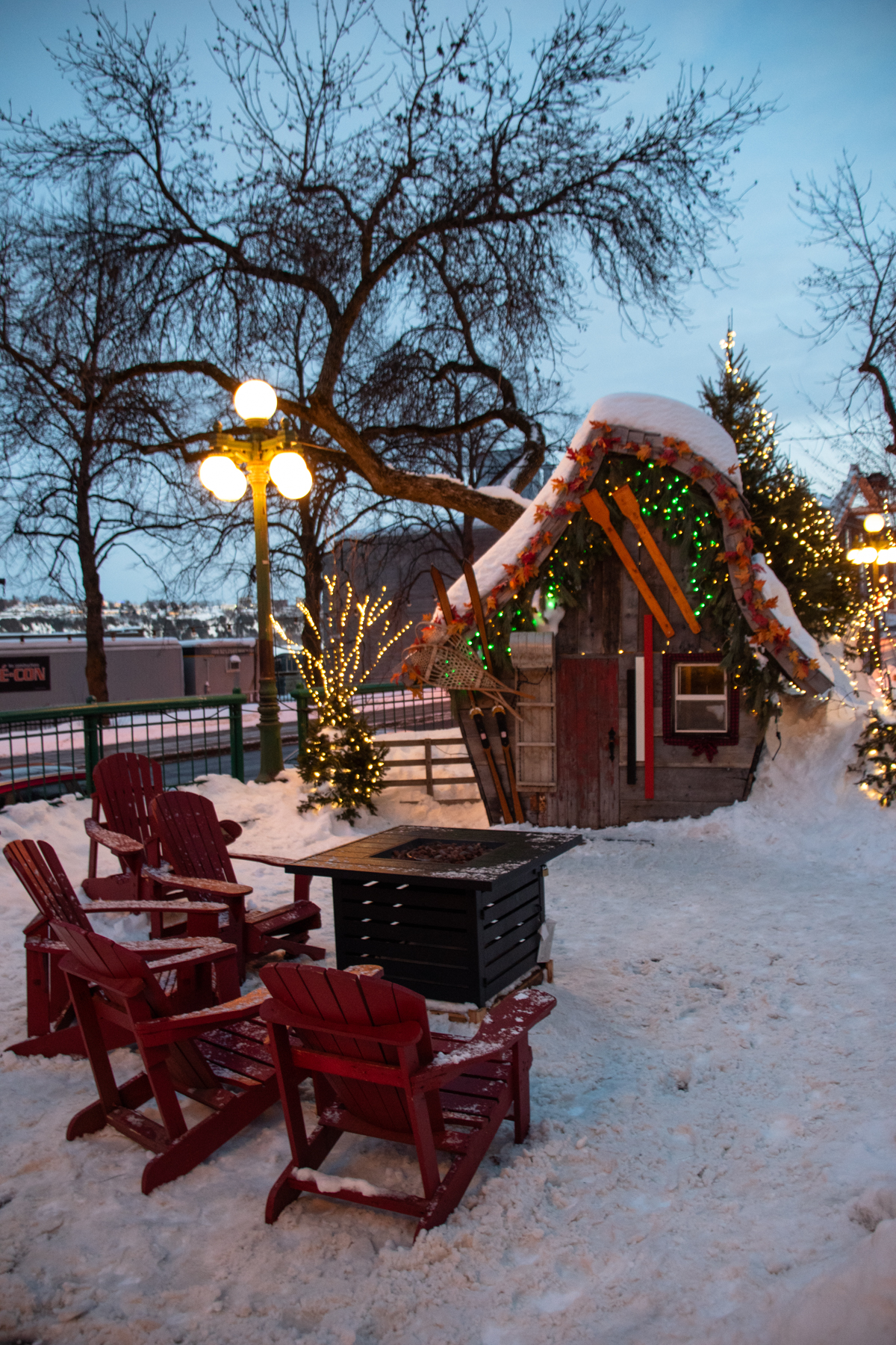 Cozy public warming station in Old Quebec with red Adirondack chairs, fire pit, and snow-covered hut decorated with winter lights