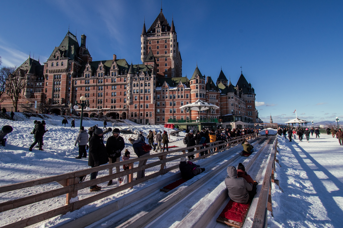 People waiting beside the Dufferin Terrace Toboggan Slide in winter with Château Frontenac in the background.