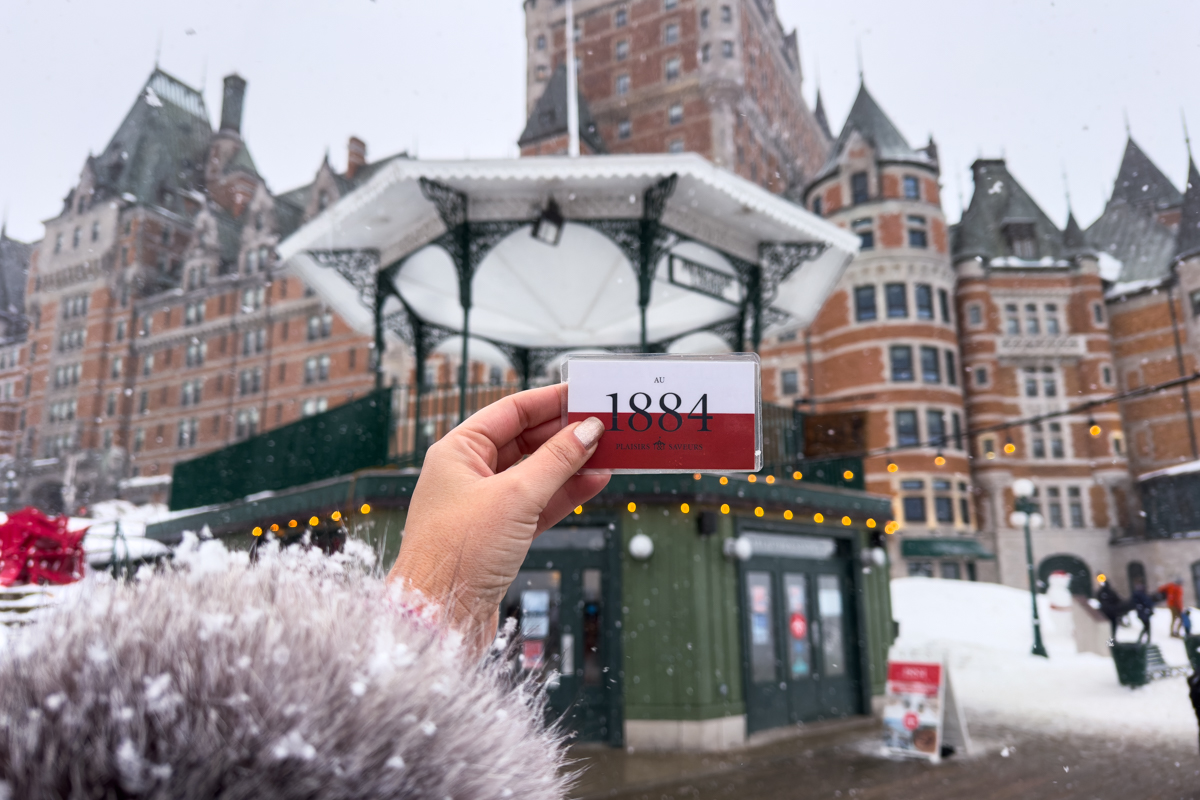 Close-up of an Au 1884 Toboggan Slide ticket held in front of Château Frontenac on a snowy day