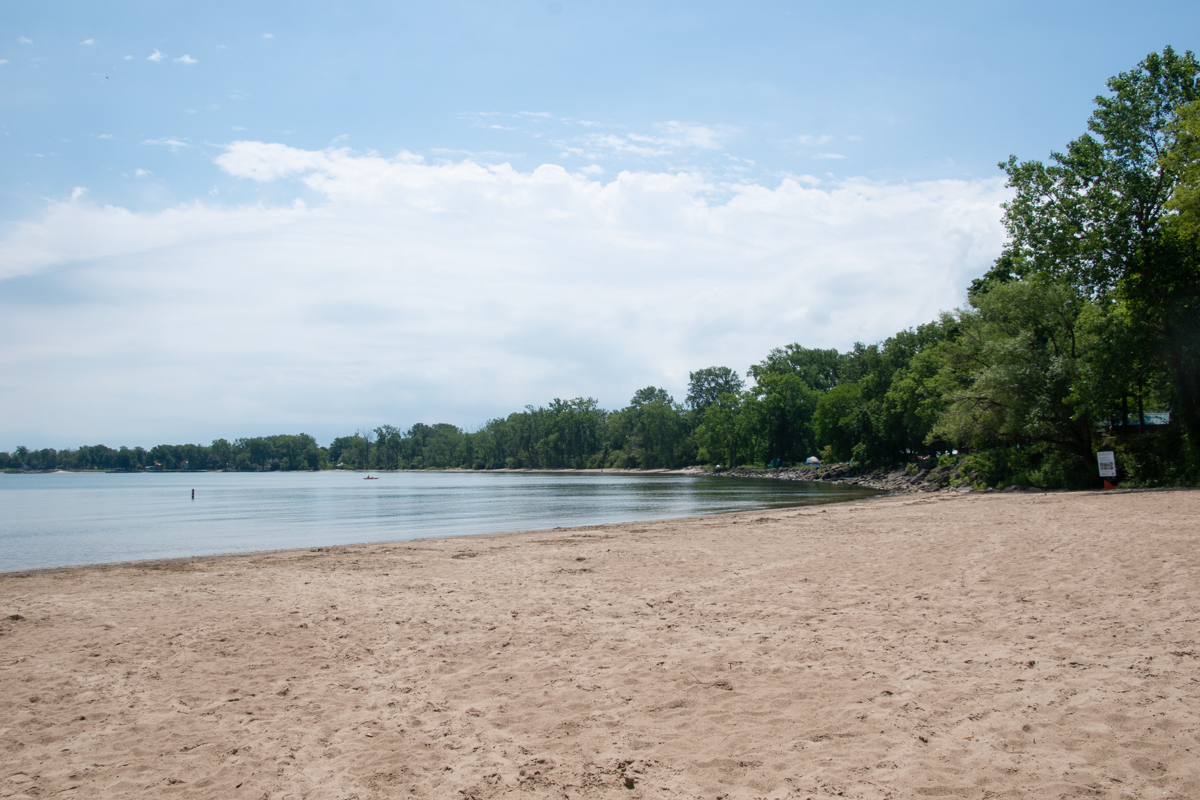 Sandy beach at Kelleys Island State Park with calm Lake Erie waters, tree-lined shoreline, and wide open views across the lake.