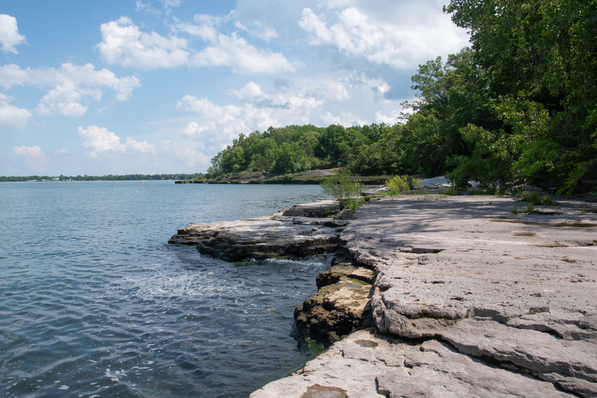 Limestone shoreline at Kelleys Island State Park overlooking Lake Erie, featuring flat rock ledges, calm water, and a forested coastline.