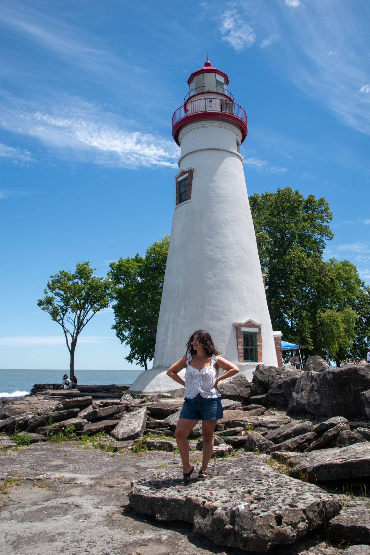 Woman (Anna Hammerschmidt from Come Join My Journey) standing in front of Marblehead Lighthouse on the rocky Lake Erie shoreline in Ohio.
