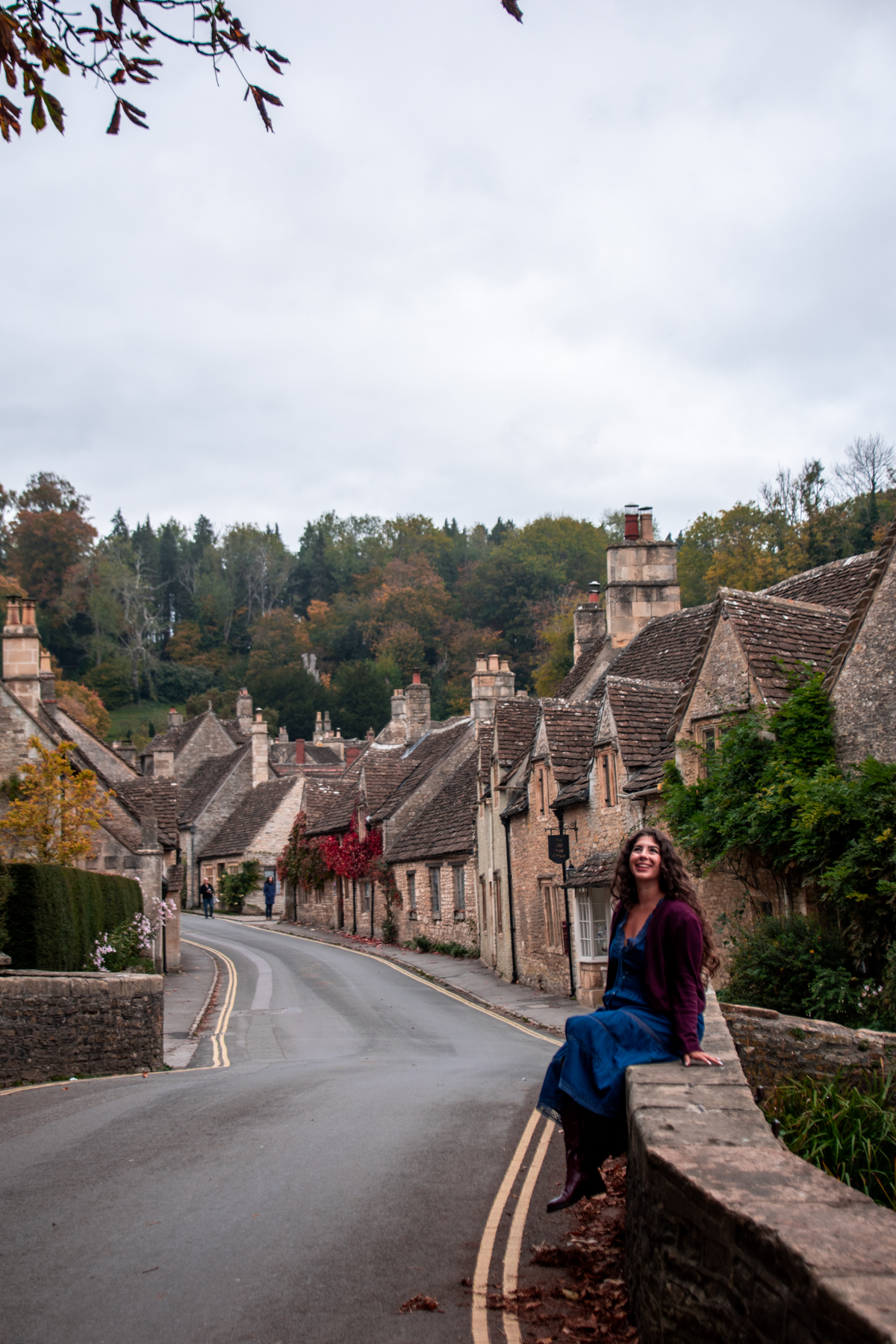 Woman sitting on a stone wall of the Castle Combe Bridge.