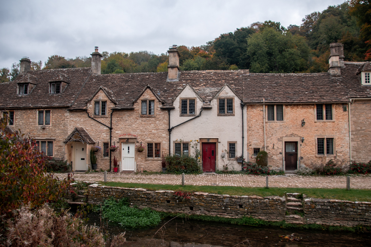 Historic cottages across the Bybrook River surrounded by early autumn foliage in Castle Combe.
