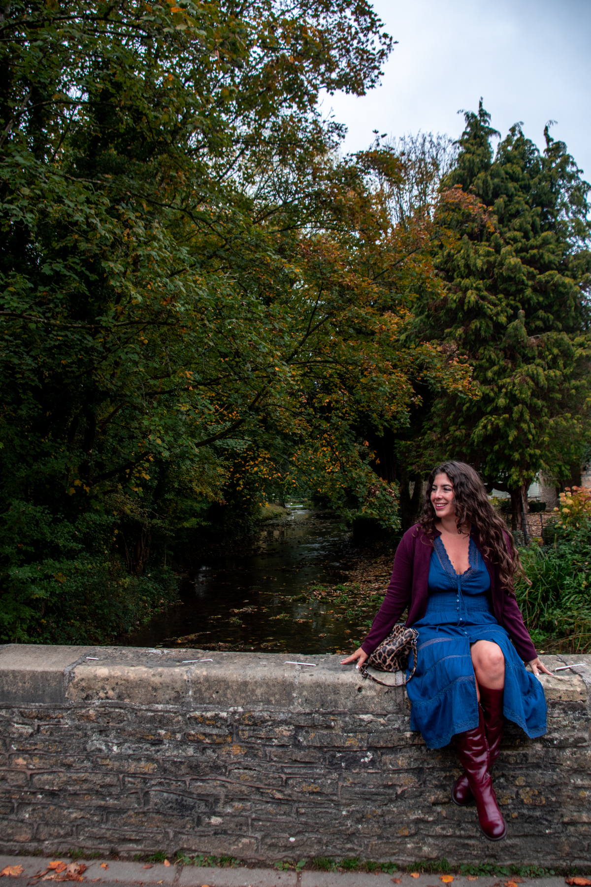 Woman sitting on the stone bridge overlooking the Bybrook River in Castle Combe.